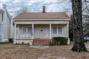 Une maison de plain-pied avec un porche à l’avant, une cheminée et un drapeau américain.