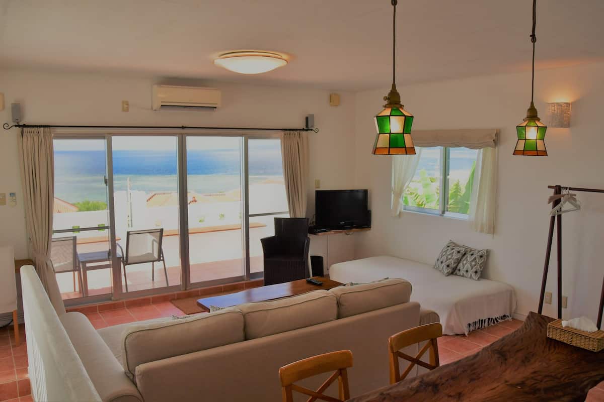 Ein Zimmer mit einer Couch, einem Fernseher, einem Esstisch und Meerblick.