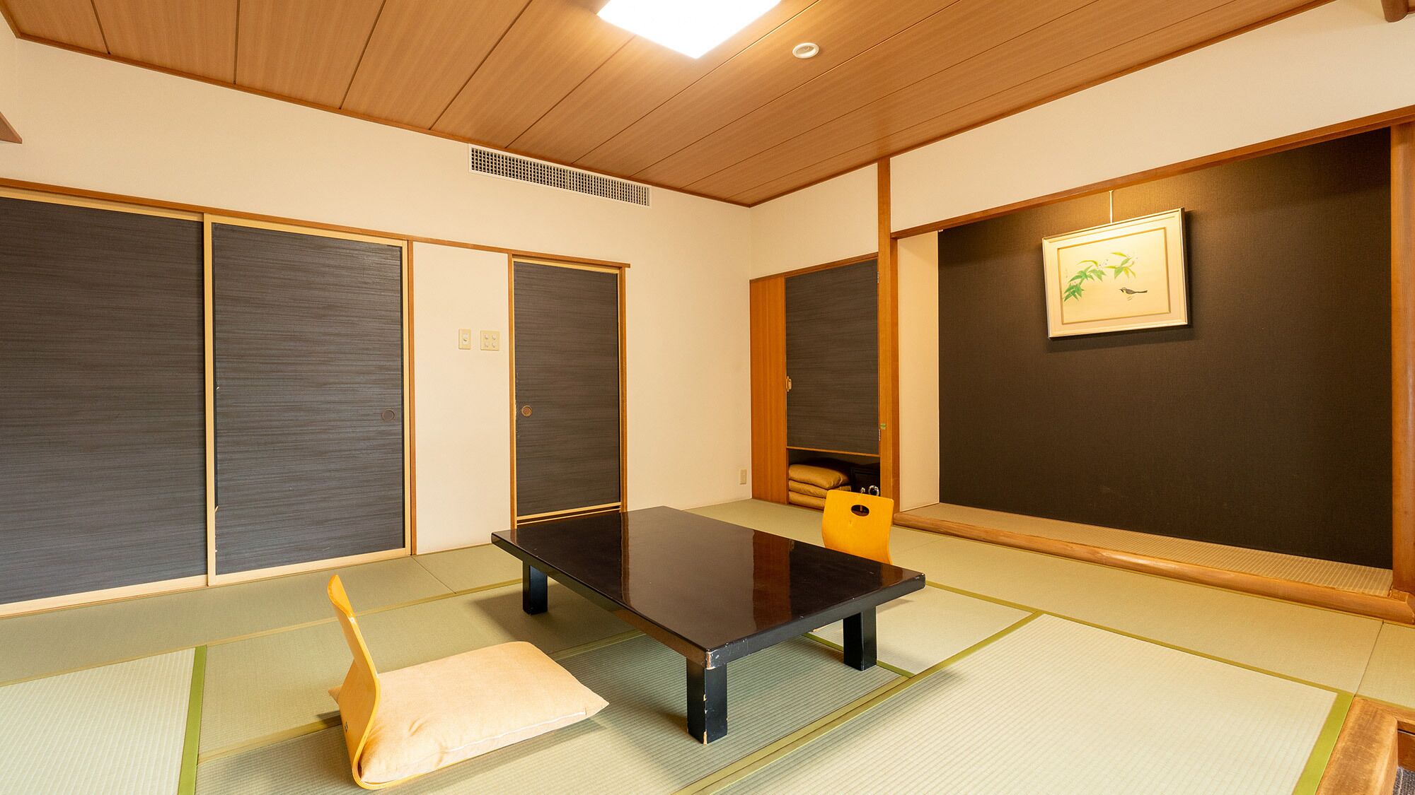 A tatami mat room with a low table and cushions, wooden sliding doors, and a framed picture on the wall.