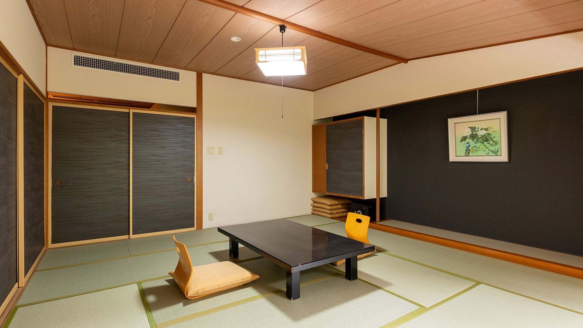 A traditional Japanese room with tatami flooring, a low table, a cushion, a cabinet, and a framed picture on the wall.