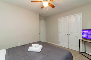 A bedroom with a bed, a ceiling fan, a television on a stand, and a door. - Near Shops, Dining & Airport- The Hilltop Bungalow (Columbus)