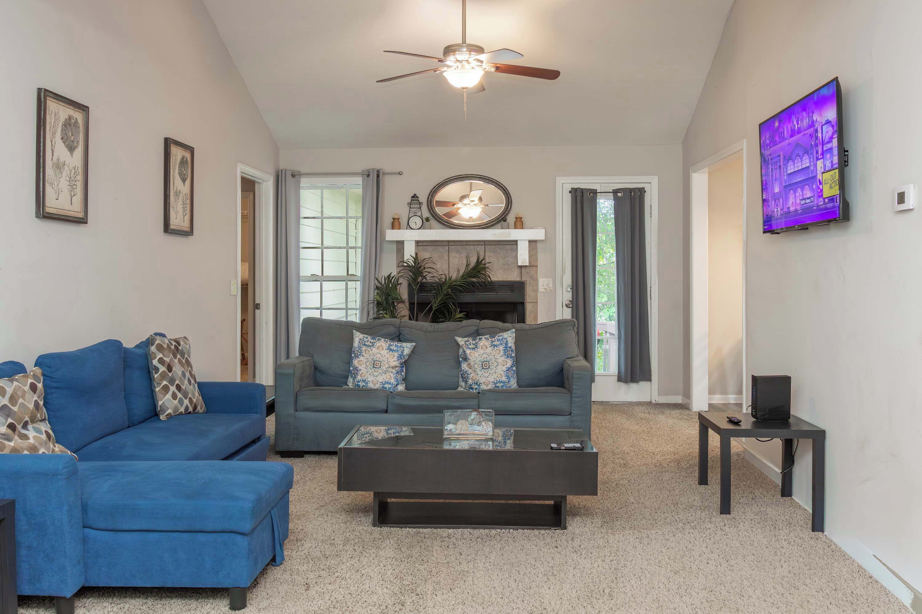 A living room with a blue sofa, a dark coffee table, a ceiling fan, a fireplace, and a mounted TV.