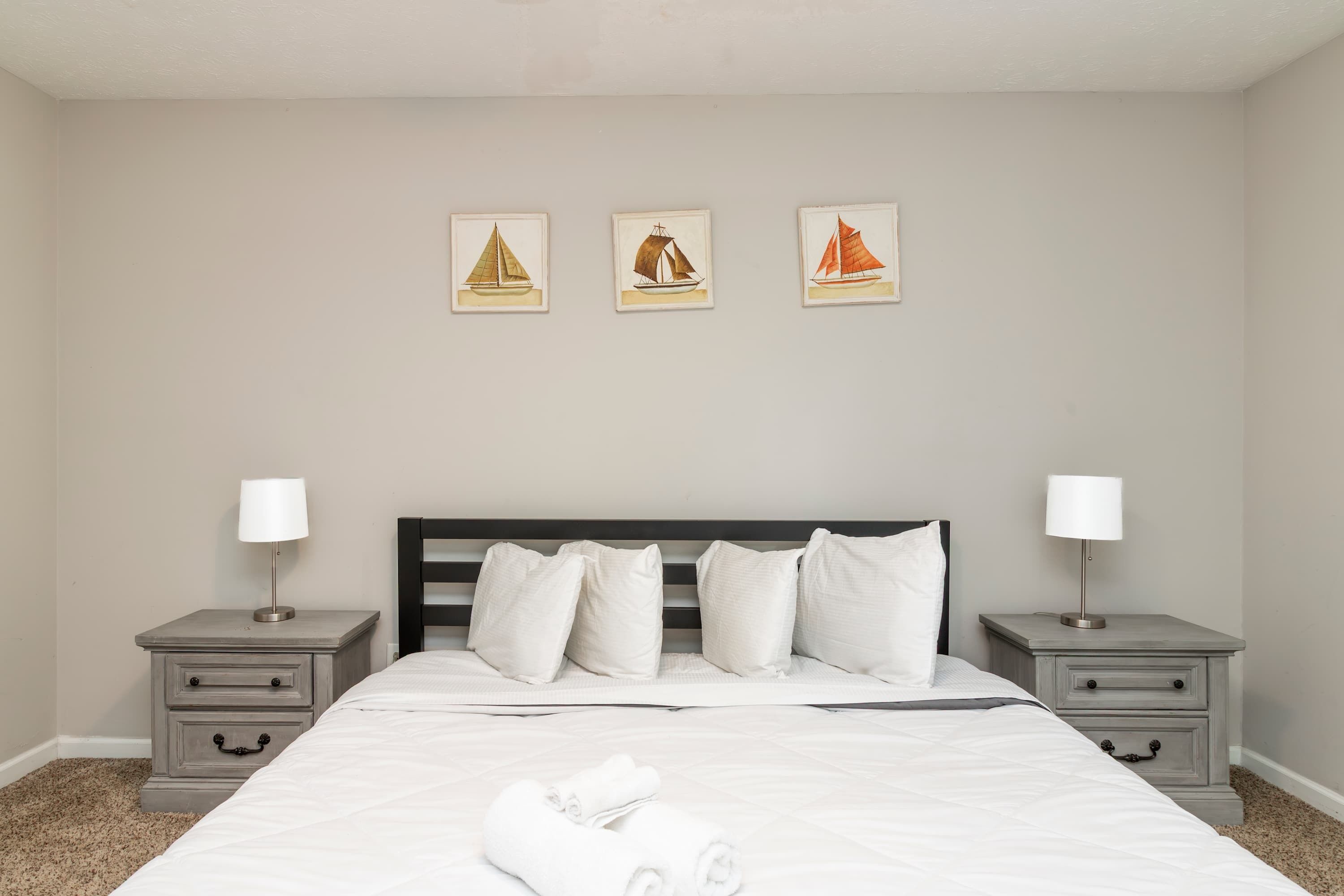 Une chambre à coucher avec un lit, deux tables de chevet et trois tableaux encadrés accrochés au mur.