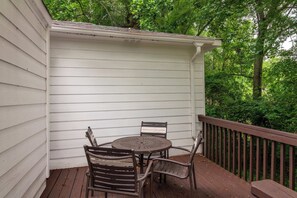 Un espace extérieur abrité, avec une table et des chaises, entouré d’une terrasse en bois et d’un mur extérieur blanc.
