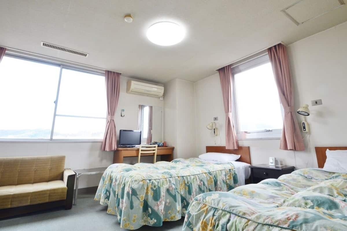 Una habitación de hotel con dos camas, un escritorio con computadora, una silla y un sofá.