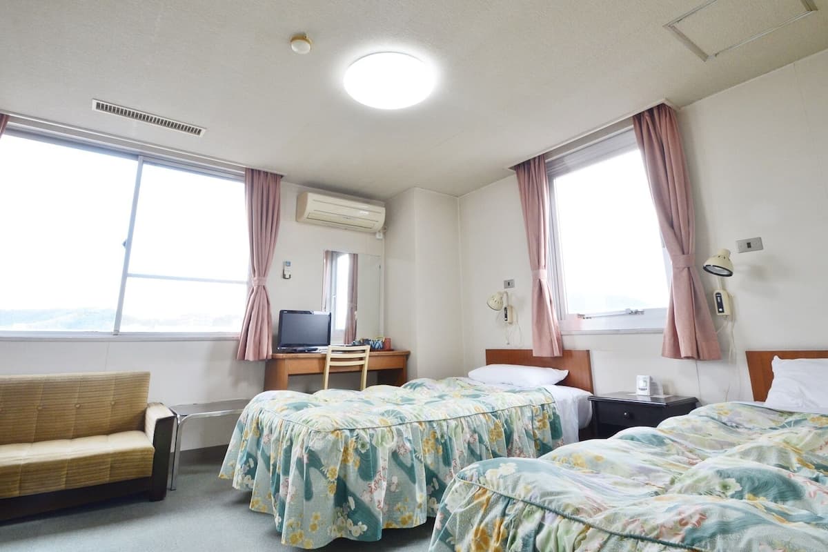 Habitación de hotel con dos camas, un escritorio, una silla, un sofá y un ventanal con cortinas.