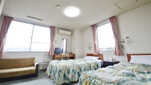 A hotel room with two beds, a desk, a chair, a couch, and a window with curtains. - Hotel Kokubunso (Kirishima)