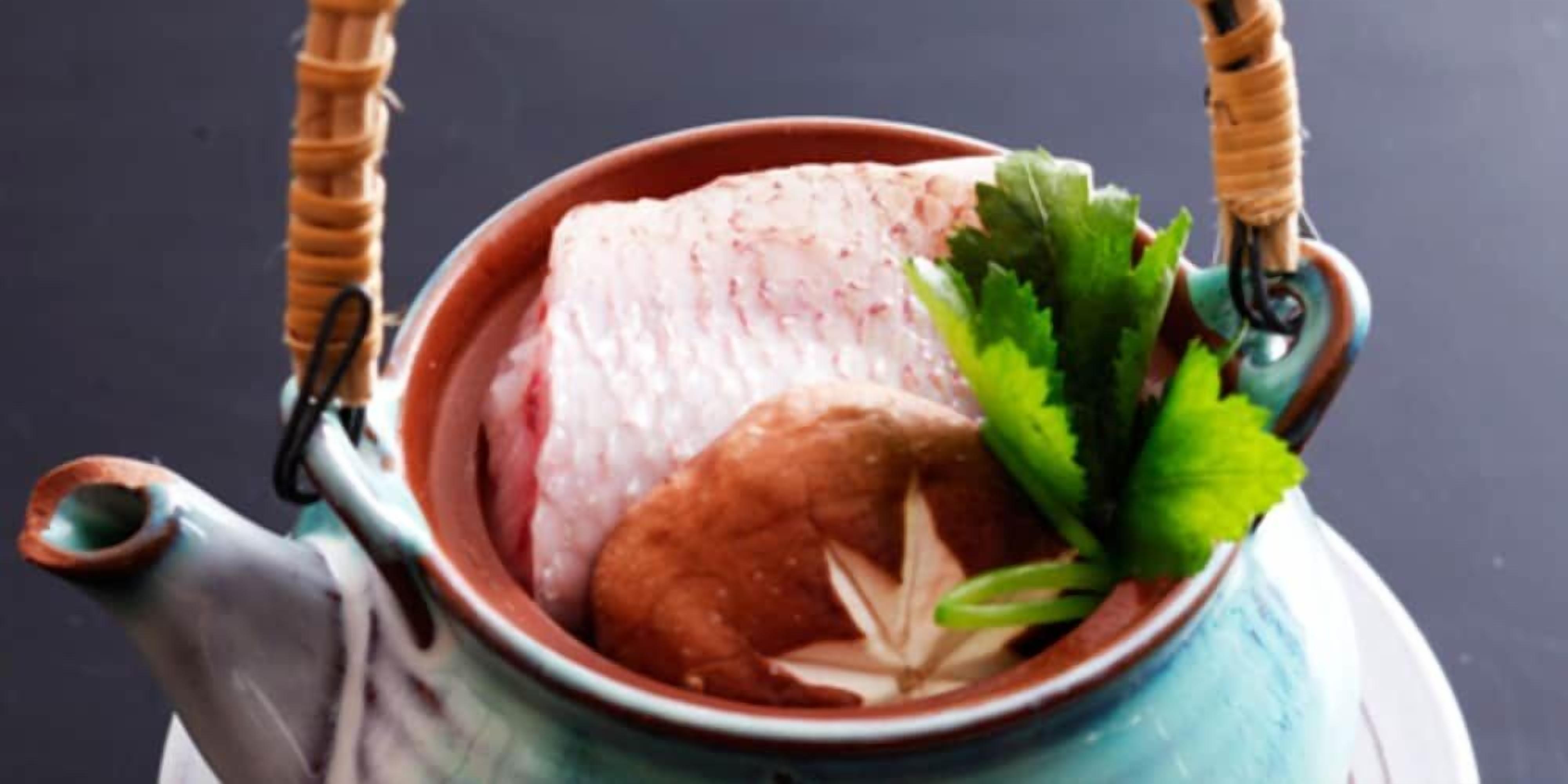 A ceramic pot with a handle, containing a piece of meat and a green leafy vegetable.