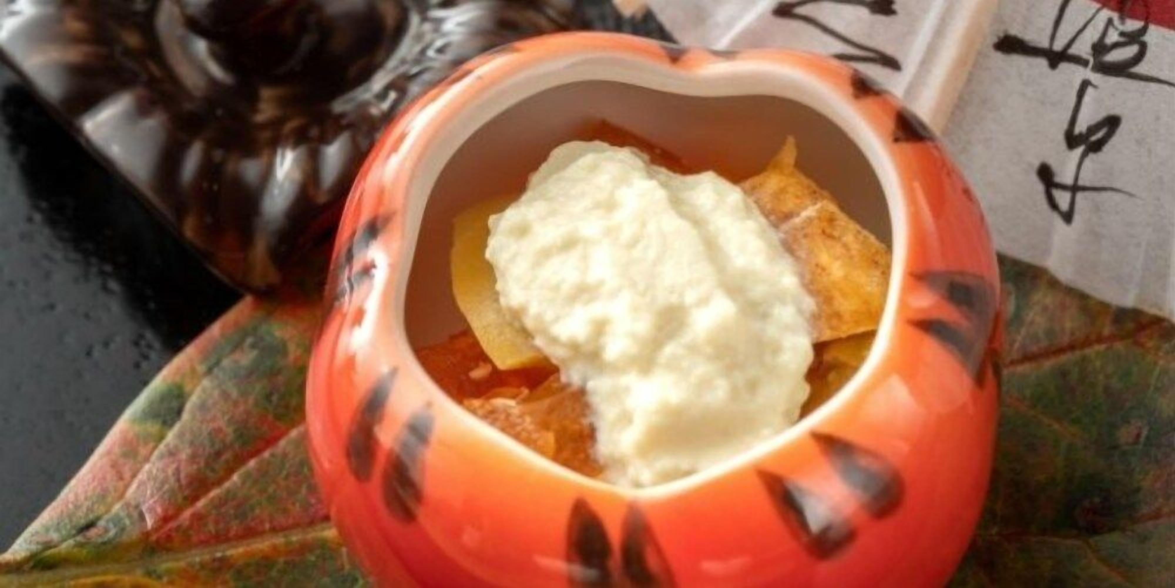 Un cuenco con forma de calabaza que contiene una sustancia cremosa blanca, posiblemente yogur o crema agria, y una porción de fruta, posiblemente manzana, sobre una hoja.