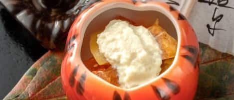 A pumpkin-shaped bowl with a white creamy substance, possibly yogurt or sour cream, and a piece of fruit, possibly apple, on a leaf.
