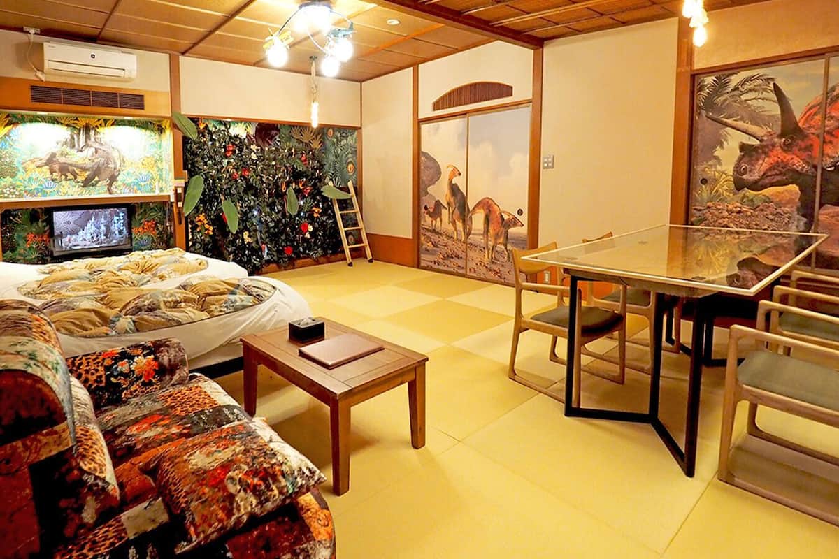 Une pièce comprenant un lit, une table à manger, des chaises, un téléviseur et des décorations sur le thème des dinosaures.