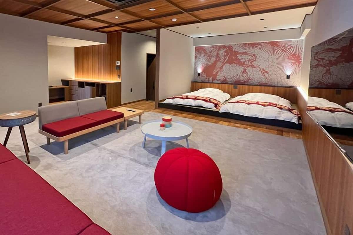 Une chambre d’hôtel moderne, dotée d’un canapé, d’une table ronde, d’un pouf rouge et d’un lit agrémenté d’une grande fresque murale.
