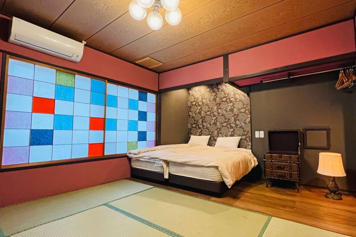 Une pièce avec un lit, un mur orné d’un motif à carreaux colorés, une commode et une lampe.
