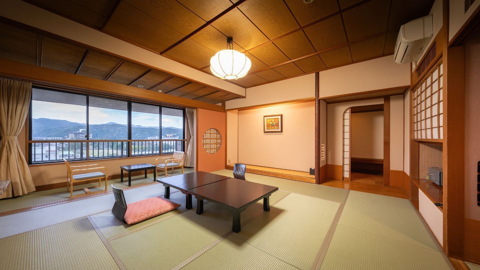 A traditional Japanese room with tatami flooring, a low table, chairs, a view through large windows, and a ceiling fan.