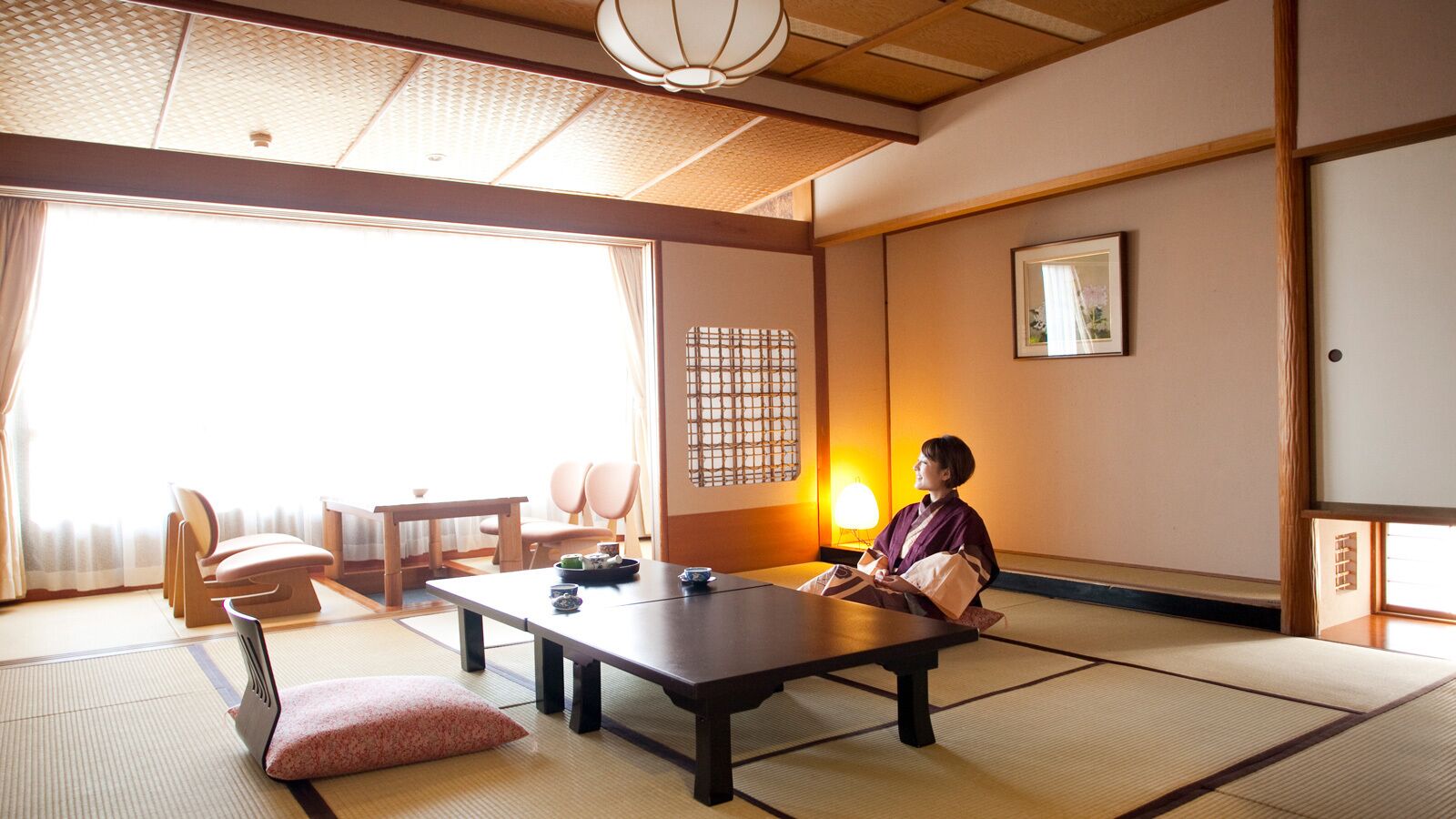 A traditional Japanese room with tatami flooring, a low table, and a person seated.