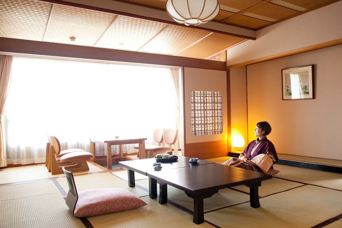 Une pièce de style japonais traditionnel, avec un sol recouvert de tatamis, une table basse et une personne assise.