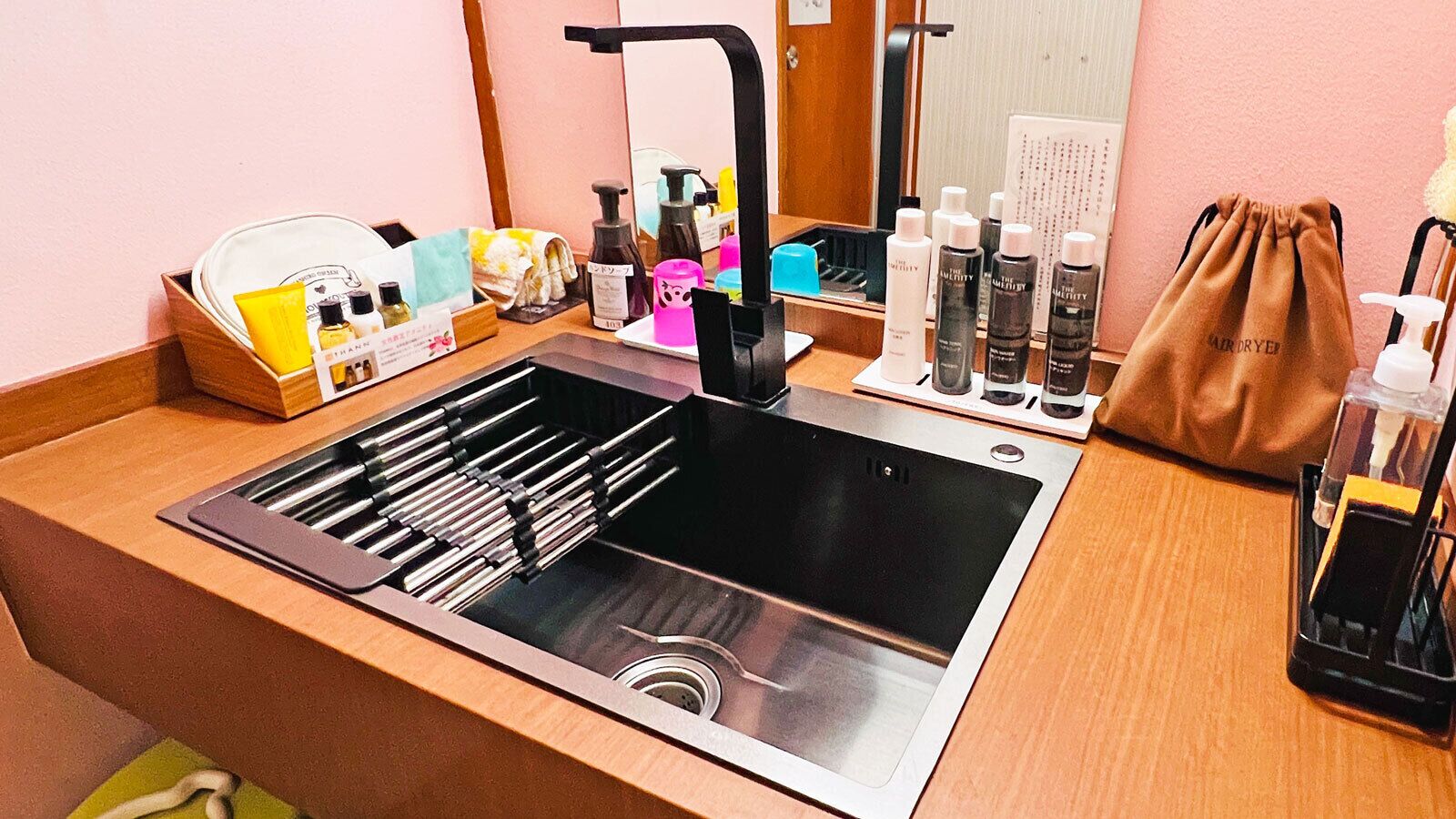 Un baño moderno con un lavamanos de acero inoxidable, un espejo y varios artículos de aseo en la encimera.