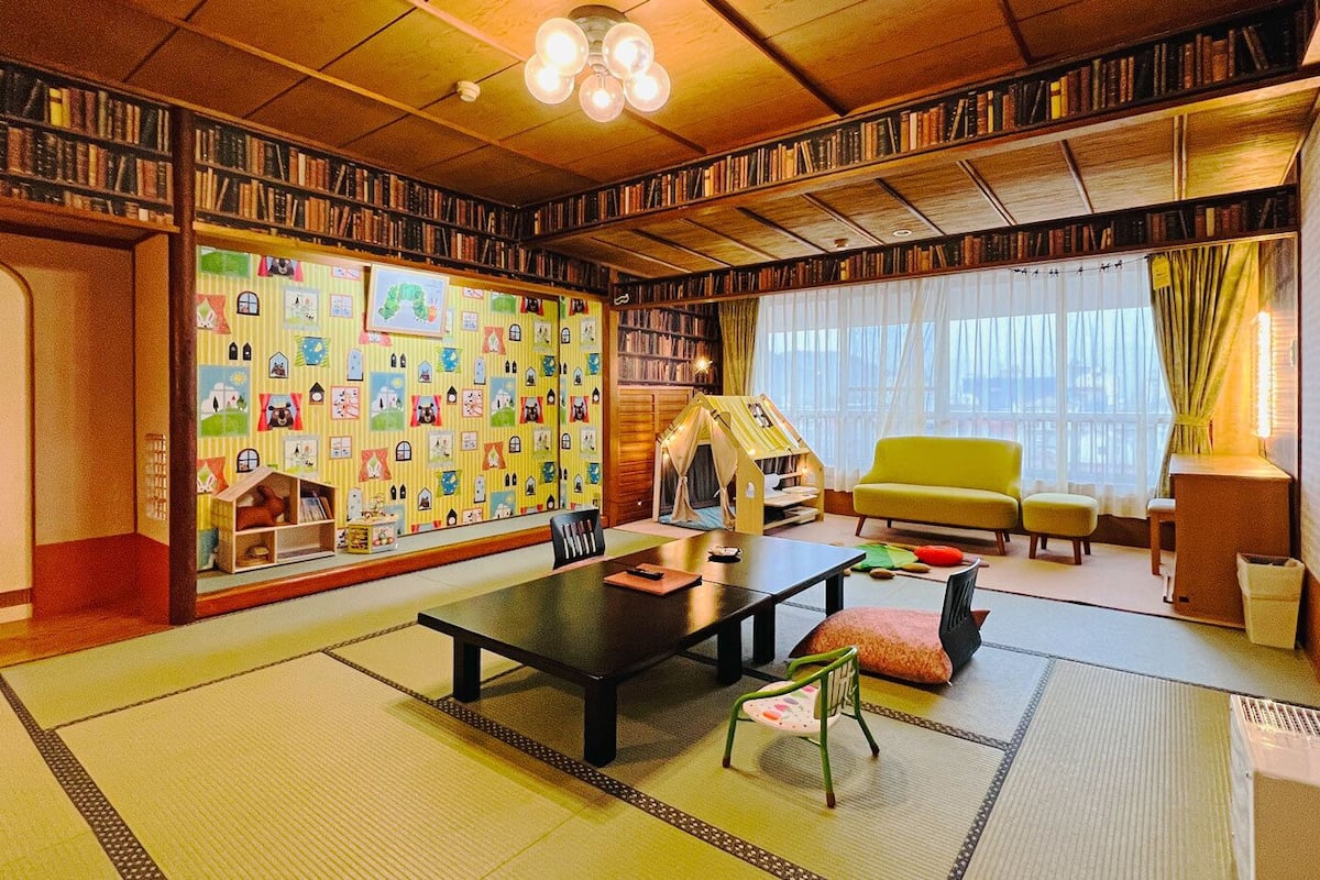 Une pièce de style japonais traditionnel, avec un sol recouvert de tatamis, une table basse, des chaises, une bibliothèque et une porte coulissante.