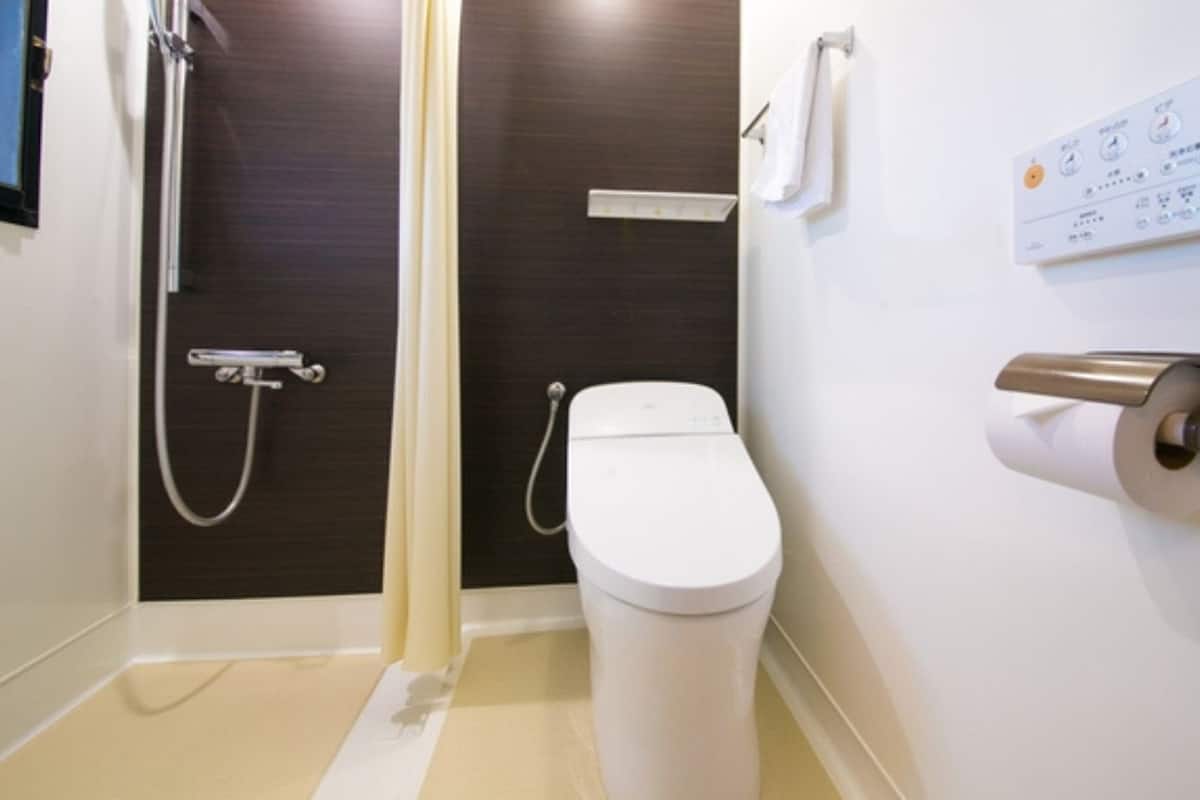 Une salle de bain équipée de toilettes, d’une douche et d’un panneau de commande fixé au mur.