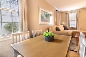 A cozy living room with a wooden dining table, a sofa, and a potted plant. - Centrally Located - The Delightful Doubles Unit B (Columbus)