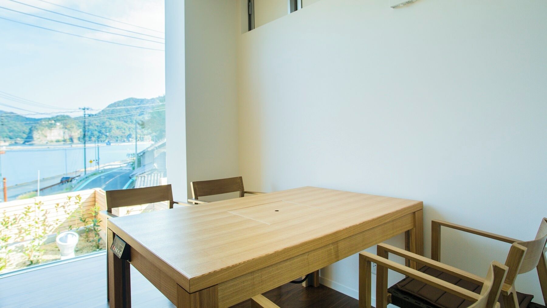 A dining area with a wooden table and chairs, a view of a body of water and hills, and a window with a power line.