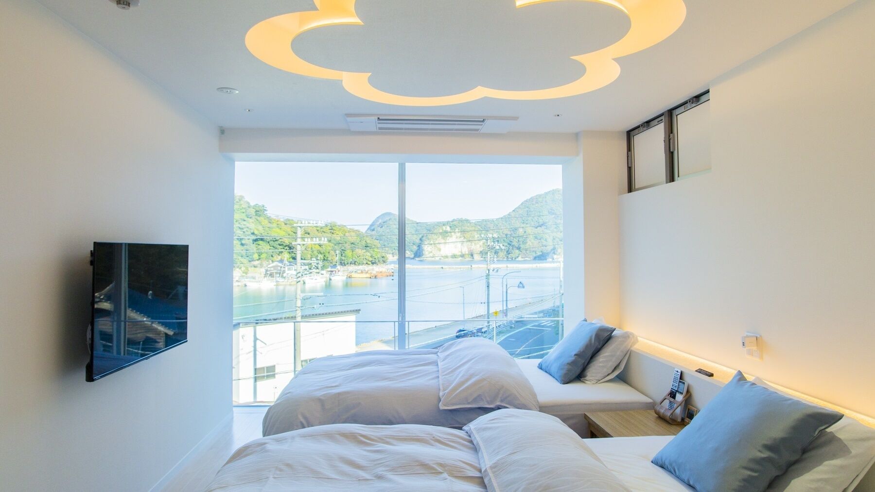A hotel room with a bed, a sofa, a TV, and a view of a body of water and hills.
