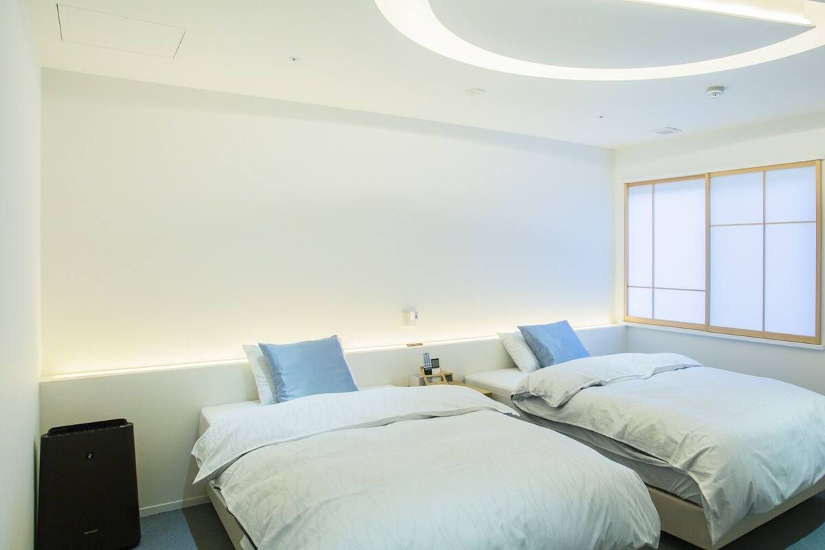 Una habitación de hotel moderna con dos camas, un ventanal grande y un diseño de techo singular.