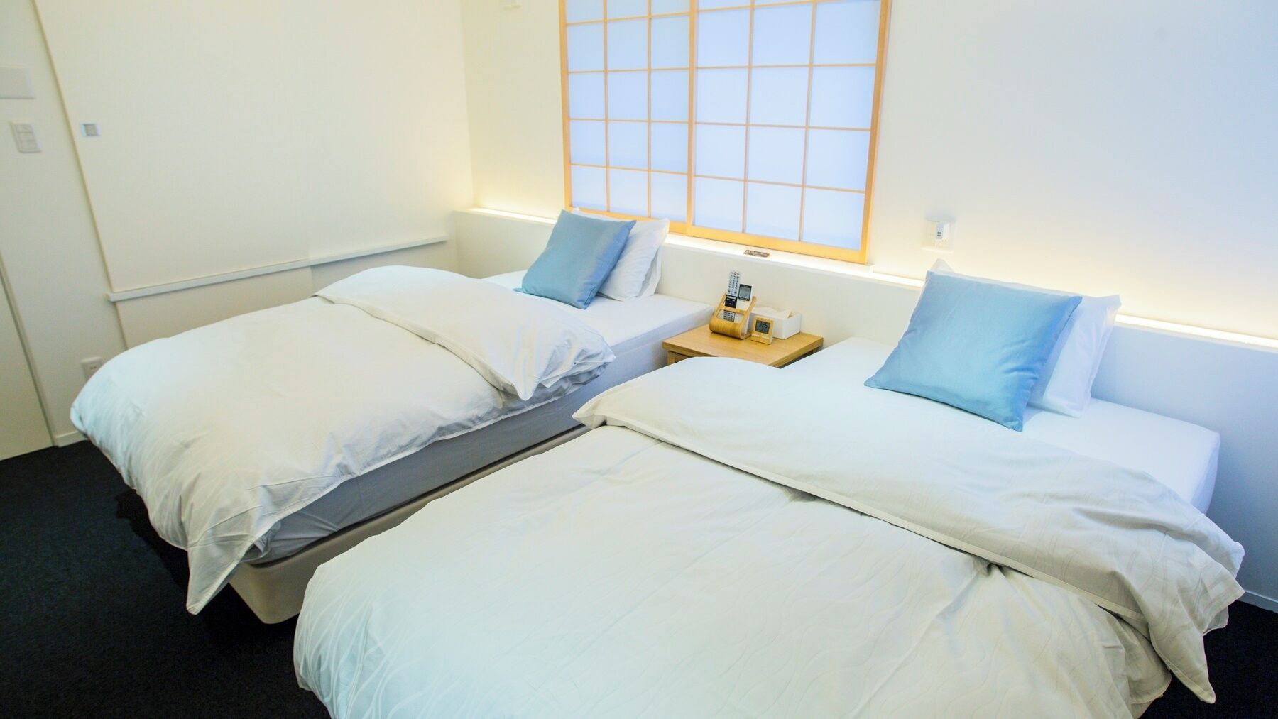 A twin room with two beds, a small bedside table with a phone, and a window with a grid pattern.