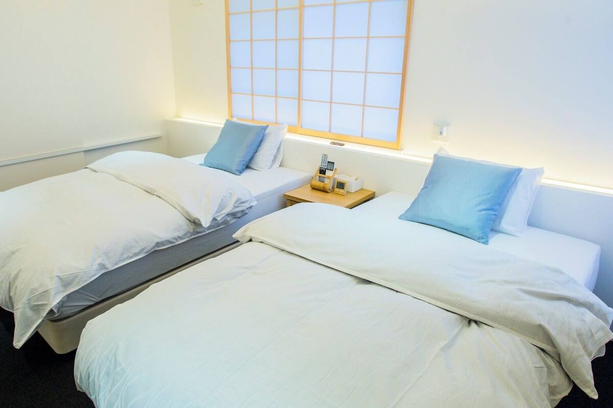 Habitación doble con dos camas, una mesita de noche pequeña con teléfono y una ventana con diseño de celosía.