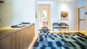 A reception area with a wooden desk, two chairs, a checkered floor, and a hallway leading to a door.