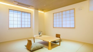 A room with a low table, two chairs, a small heater, and large windows.