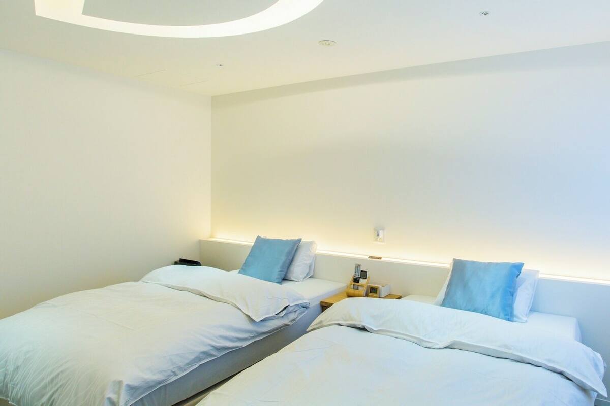Una habitación de hotel moderna con dos camas, una mesita de noche con lámpara y un ventanal amplio.