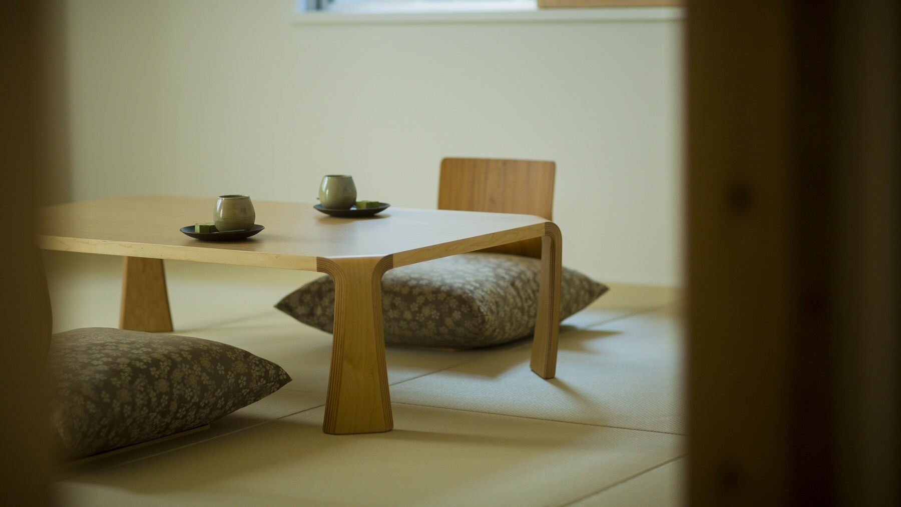 A traditional Japanese tatami mat room with a low wooden table, two cushions, and a small tea set.