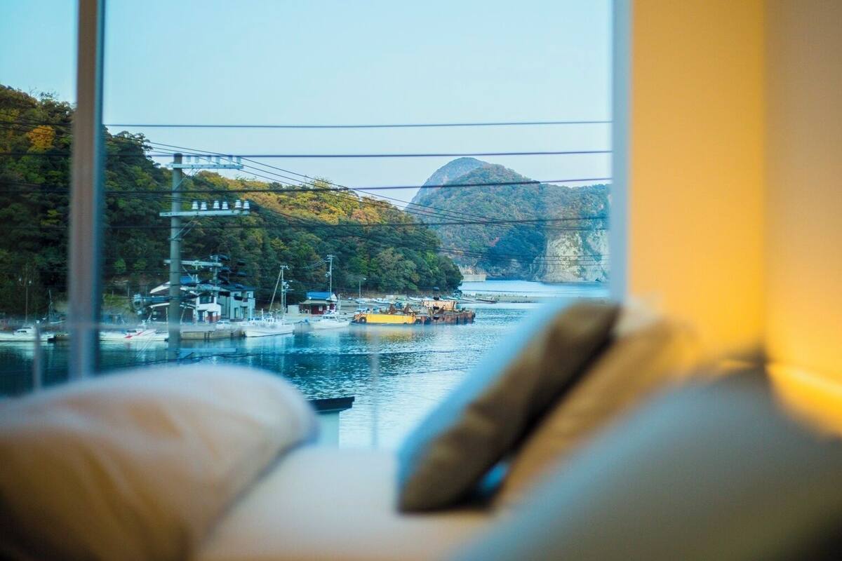 Vista desde una ventana con un sofá, un río, barcos y un puente.