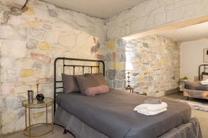 A bedroom with a stone wall, a metal bed frame, a bedside table with a lamp, and a small plant. - The Dinglewood Castle An Unparalleled Experience (Columbus)