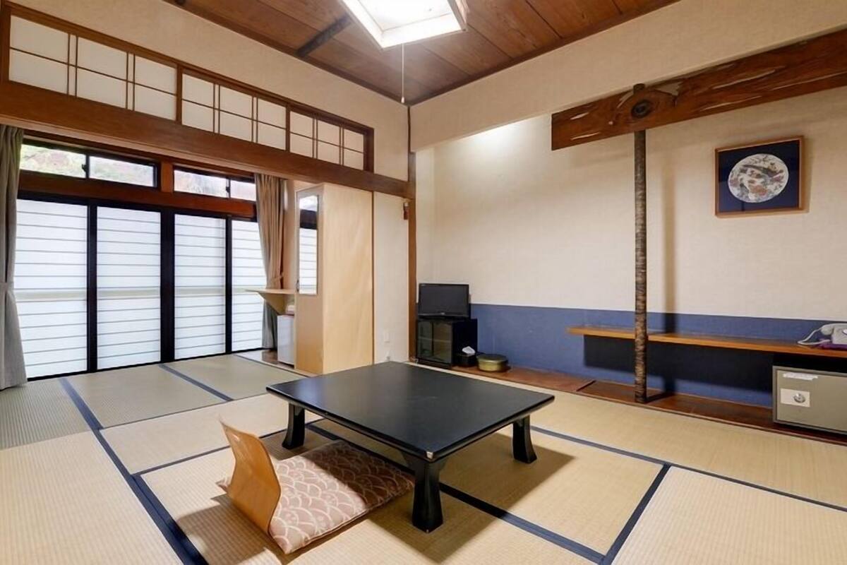 A tatami mat room with a tatami mat table, a television, and a cabinet.