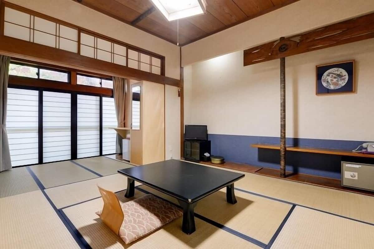 A tatami mat room with a tatami mat table, a television, and a cabinet.