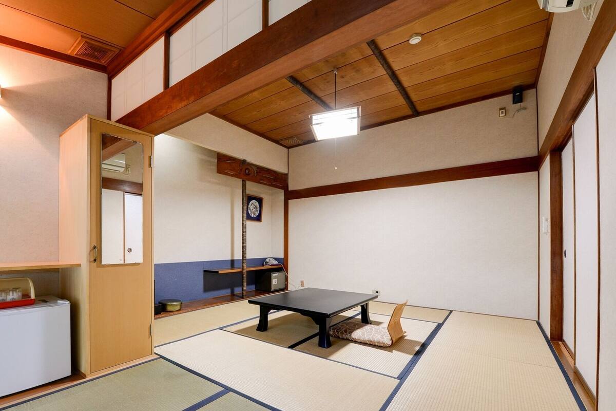 A traditional Japanese room with tatami flooring, a low table, a refrigerator, and a mirror.
