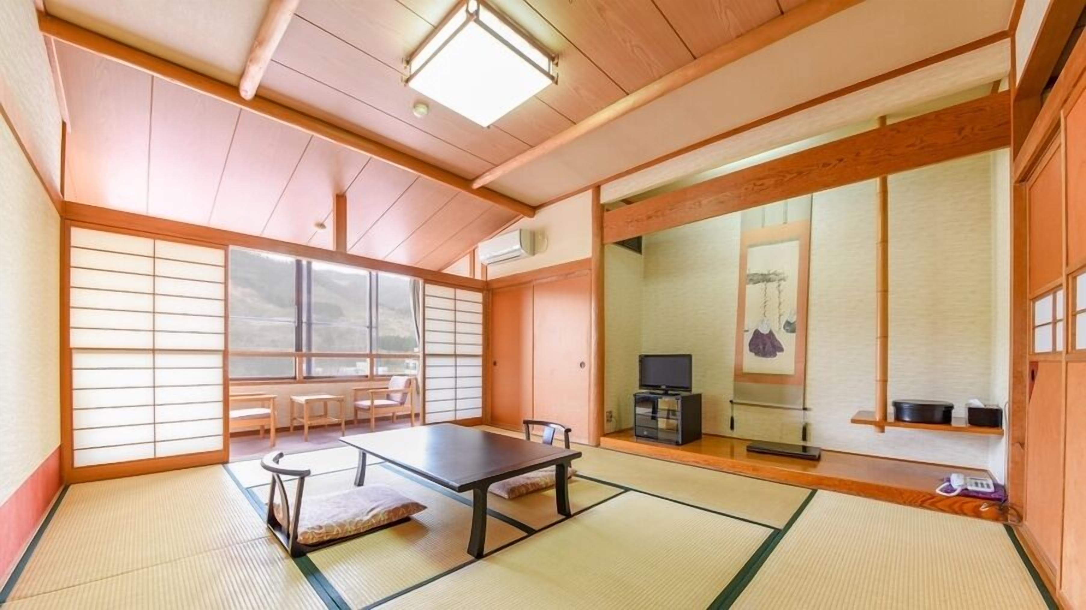 A traditional Japanese room with tatami flooring, a low table, chairs, a television, and sliding doors.
