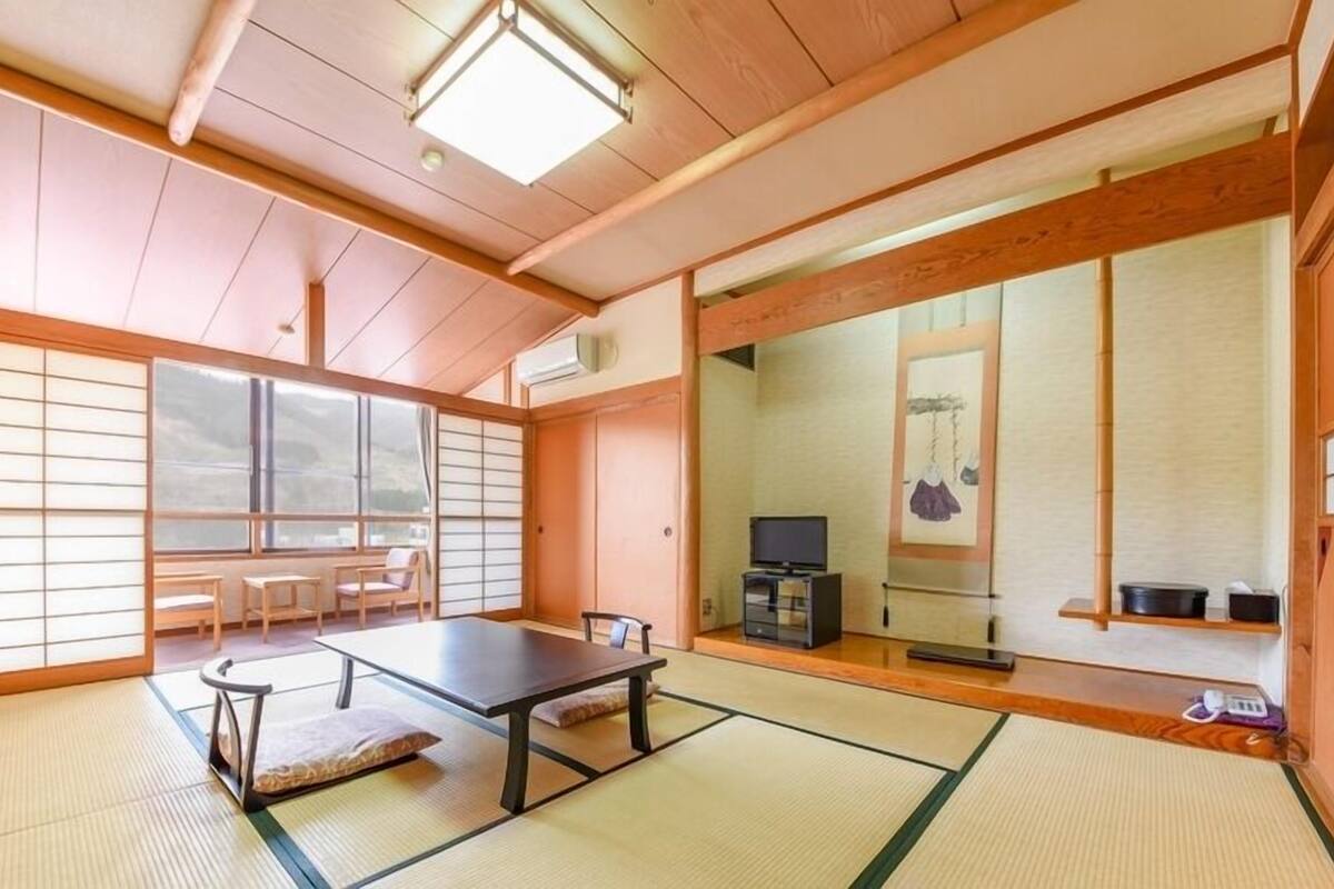 A traditional Japanese room with tatami flooring, a low table, chairs, a television, and sliding doors.