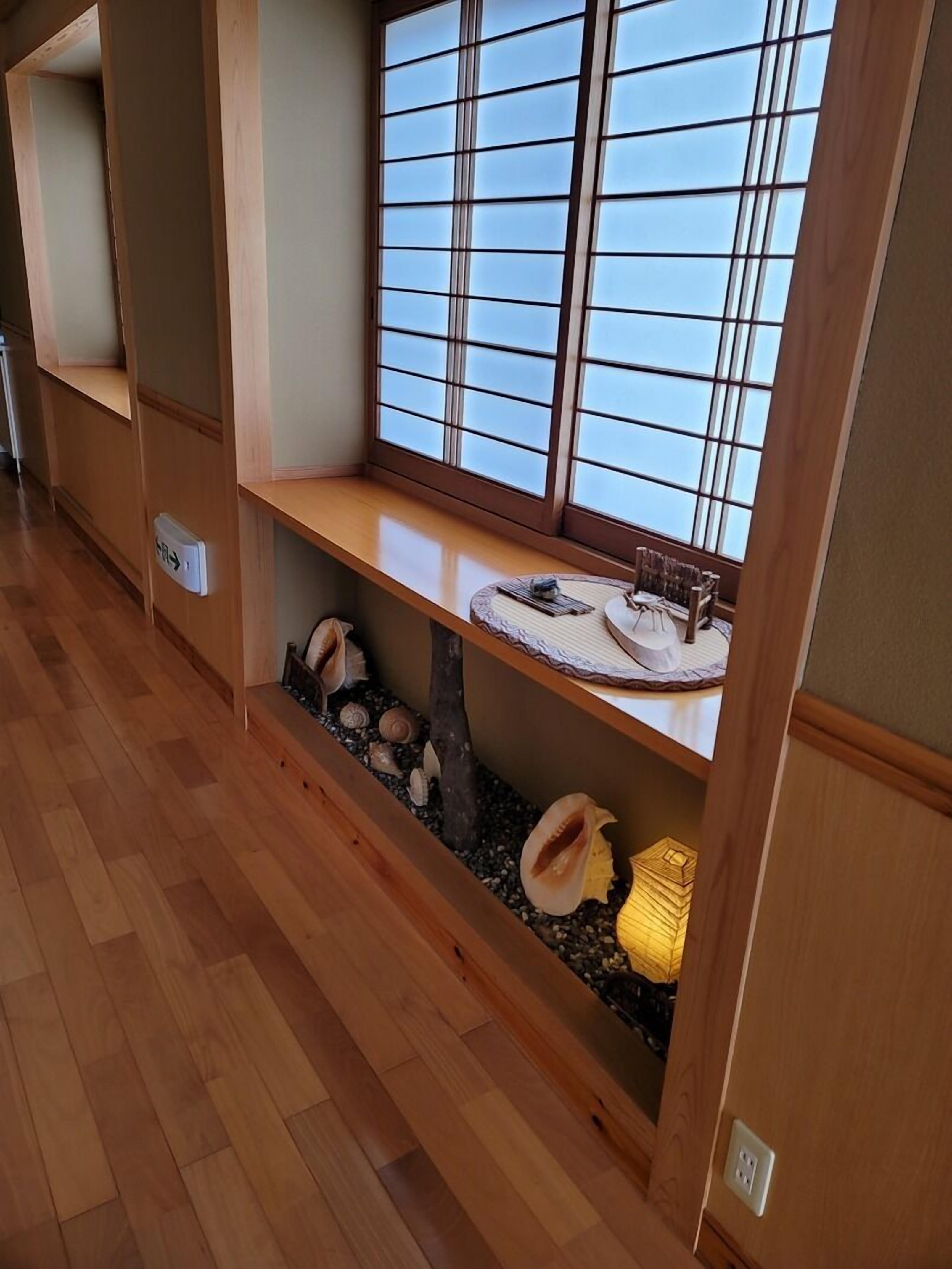 A room with wooden flooring, a window with a view, a shelf with decorative items, and a small water feature.