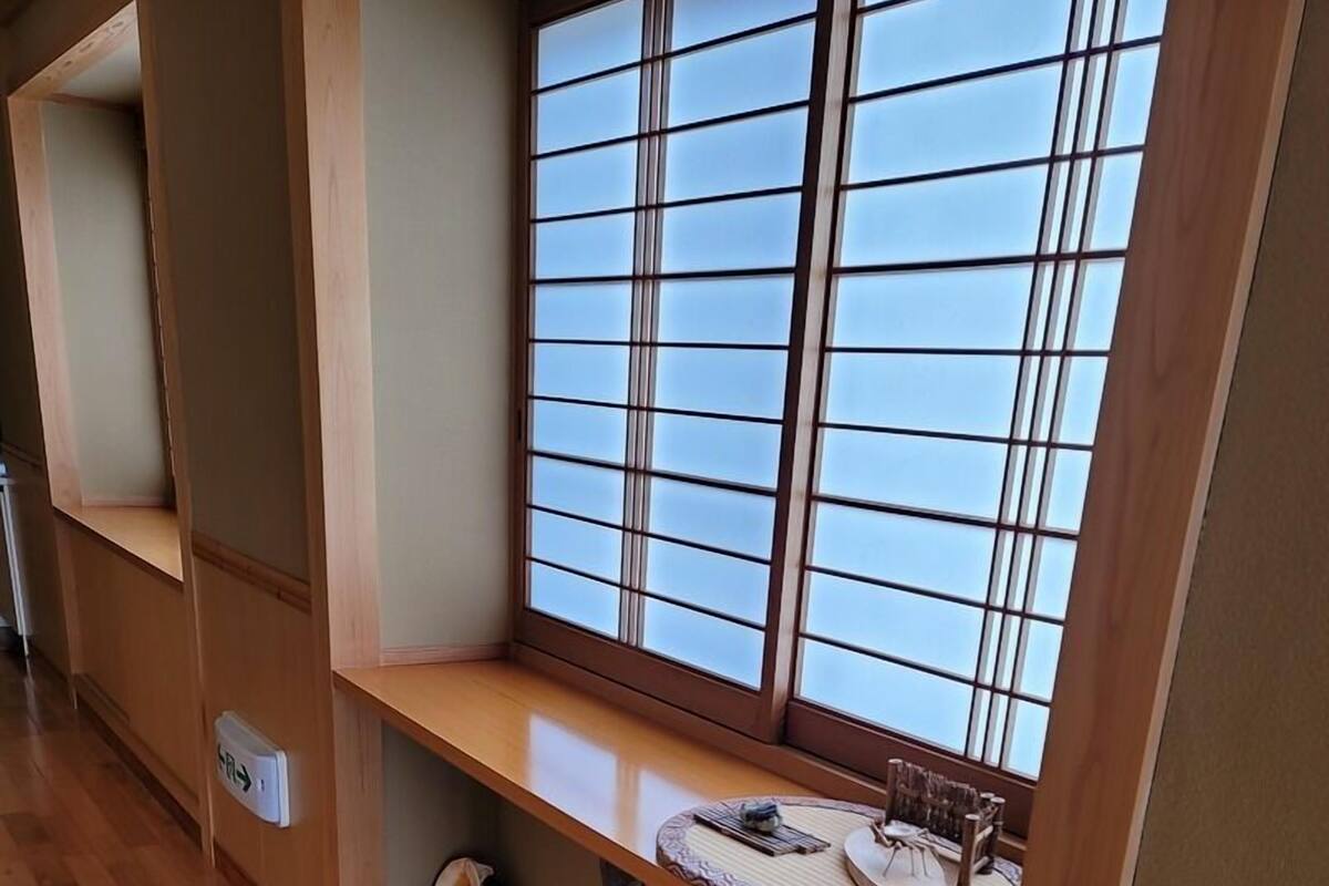 Una habitación con piso de madera, una ventana con vista, un estante con adornos y una pequeña fuente de agua.