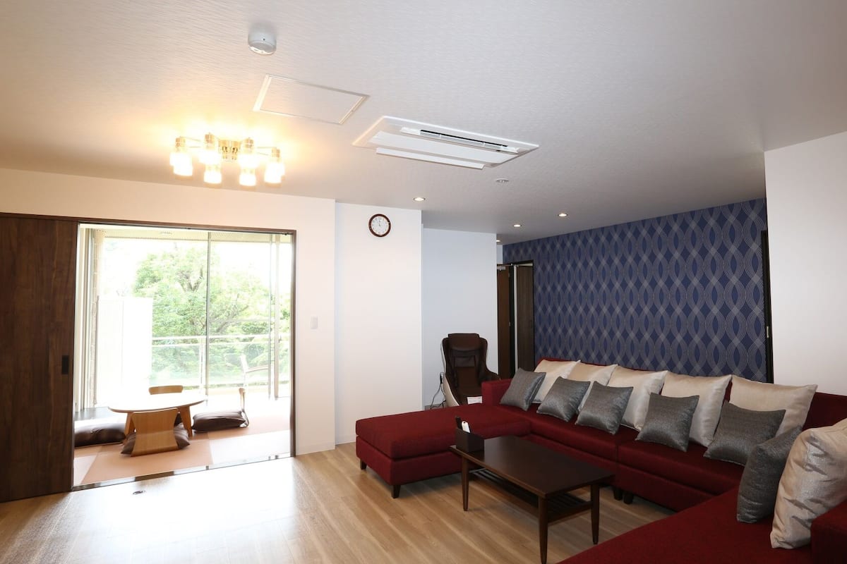 A living room with a red sofa, a coffee table, a wall clock, and a patterned wallpaper.