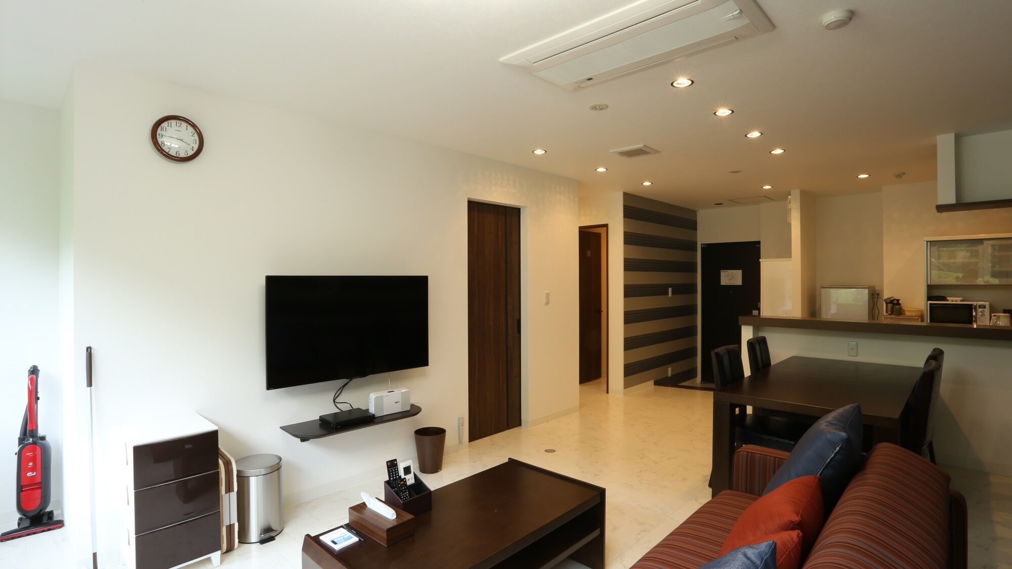 A modern living room with a flat-screen TV, a coffee table, a sofa, a dining area, and a kitchen with a microwave.