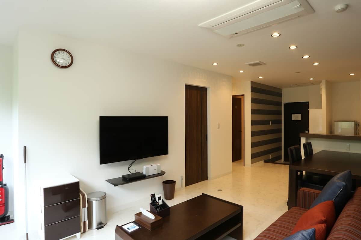 A modern living room with a flat-screen TV, a coffee table, a sofa, a dining area, and a kitchen with a microwave.