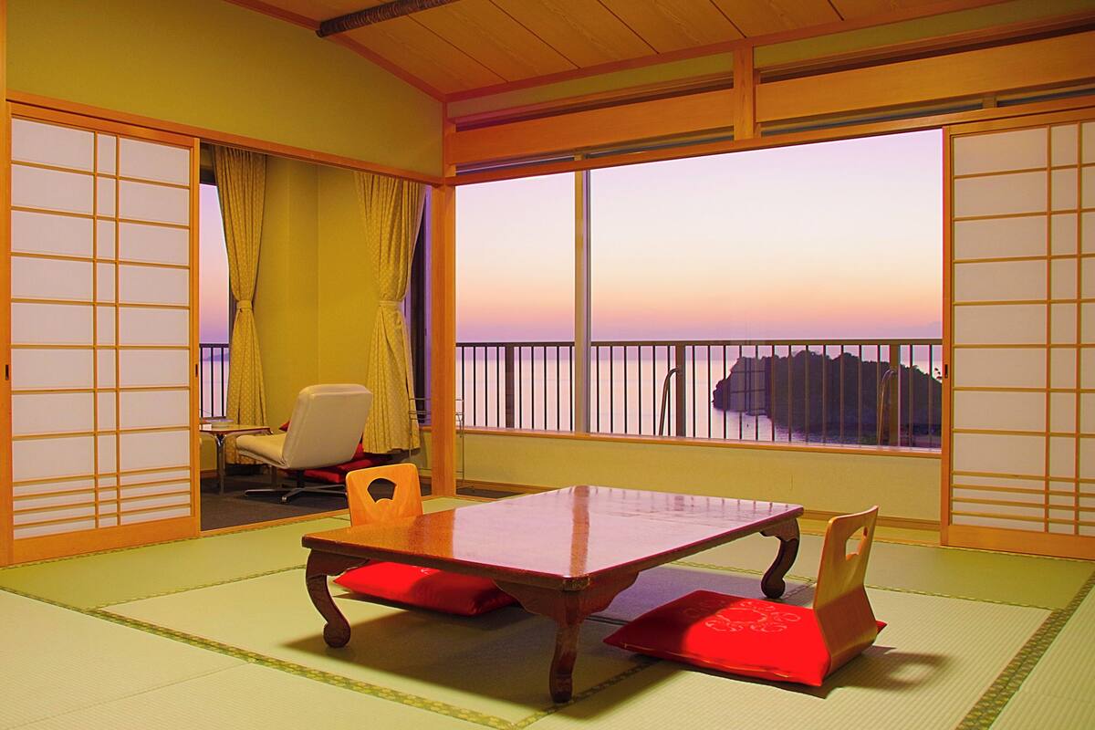 Una habitación japonesa tradicional con suelo de tatami, una mesa baja y vista al mar.