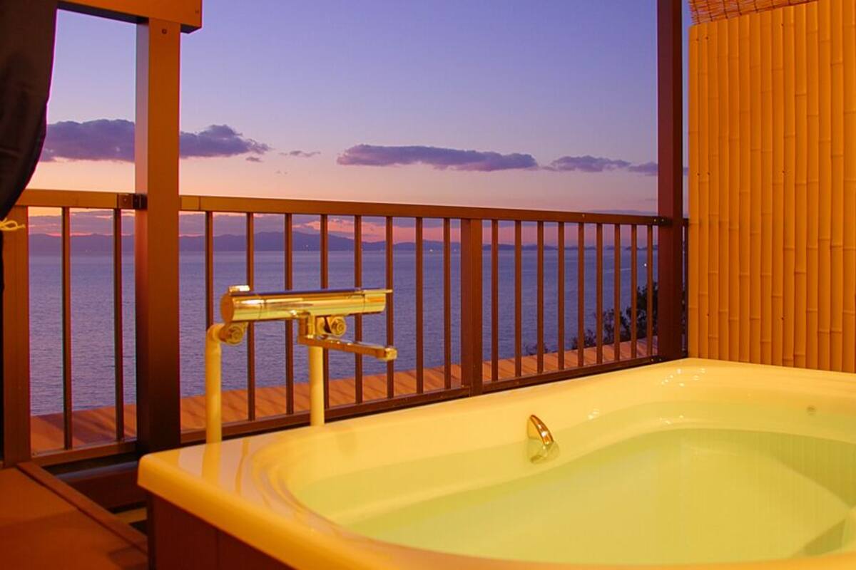 Un balcón con vista al mar, una bañera y una pared de bambú.