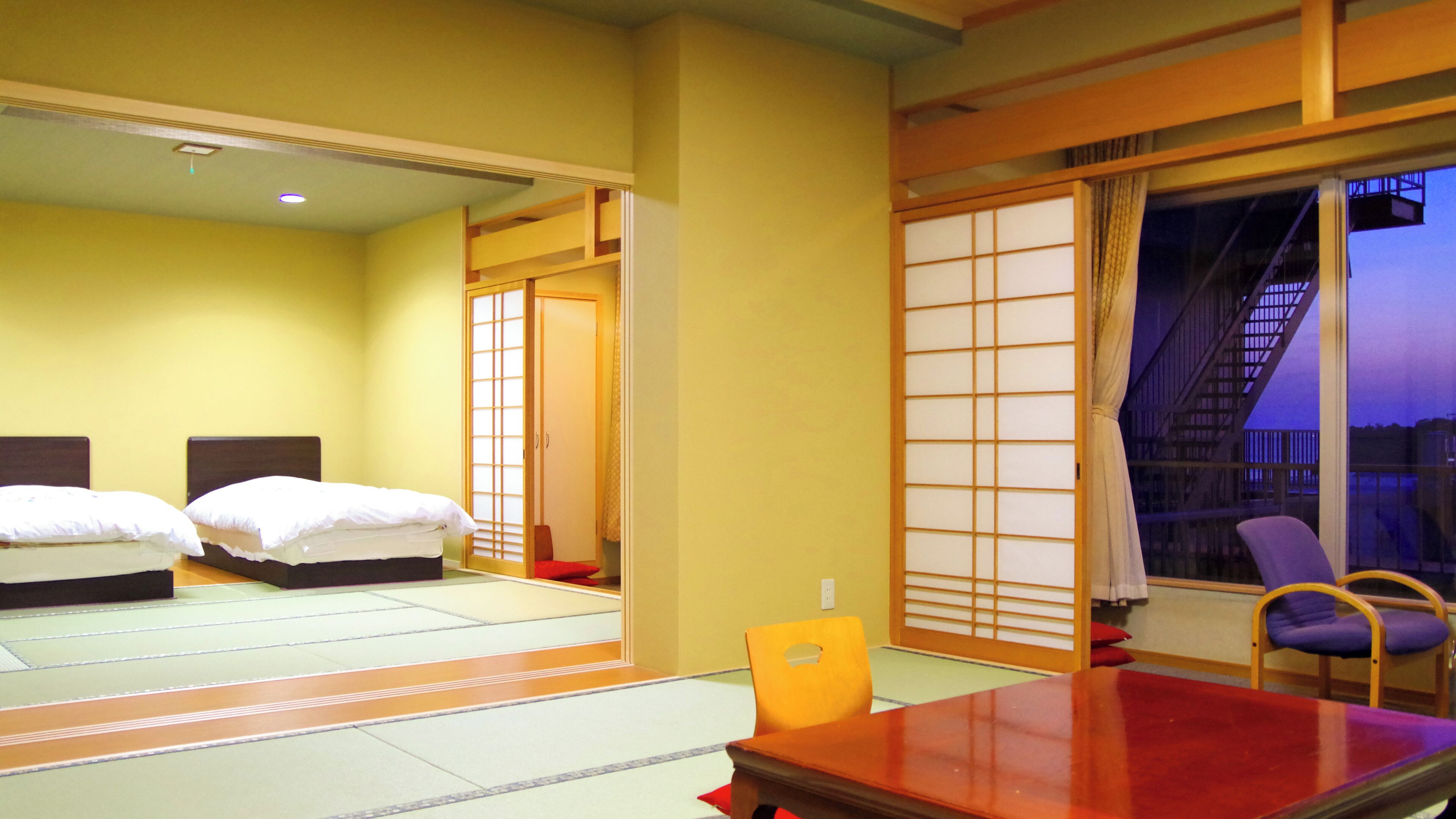 Een hotelkamer met twee bedden, een houten tafel, een stoel en een schuifdeur van shoji-papier.