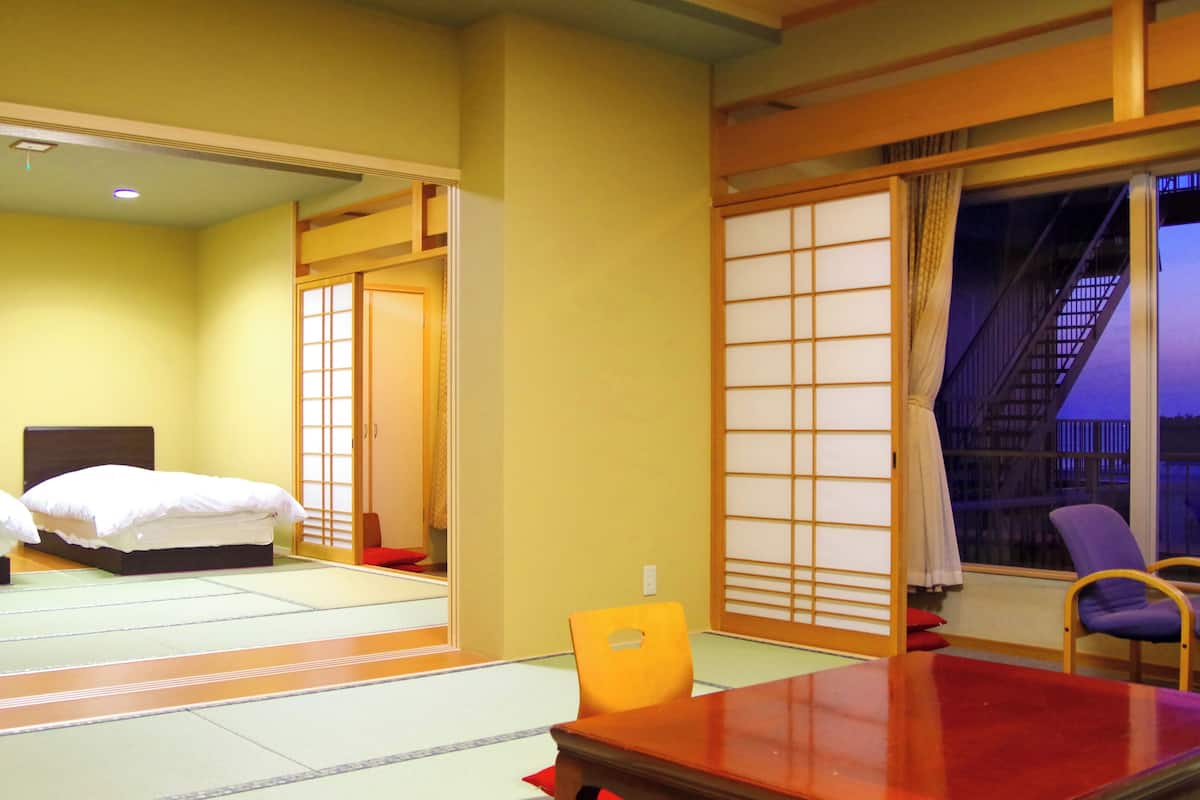 Habitación de hotel con dos camas, una mesa de madera, una silla y un panel corredizo shoji.