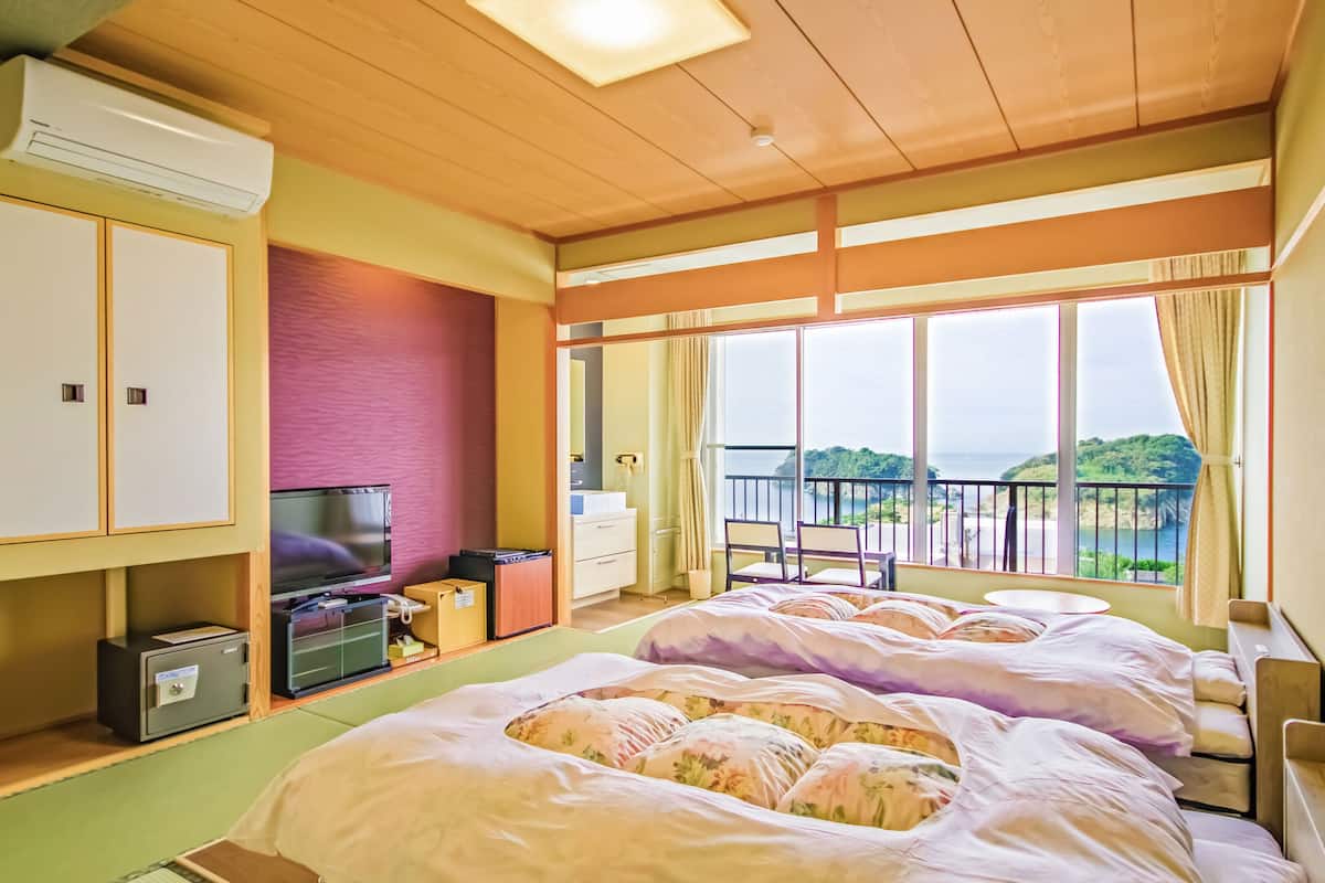 Habitación de hotel con dos camas, televisión, escritorio y balcón con vistas.
